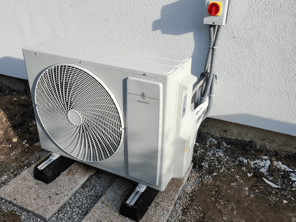 Unité extérieure de pompe à chaleur air/air installée contre un mur avec support au sol.